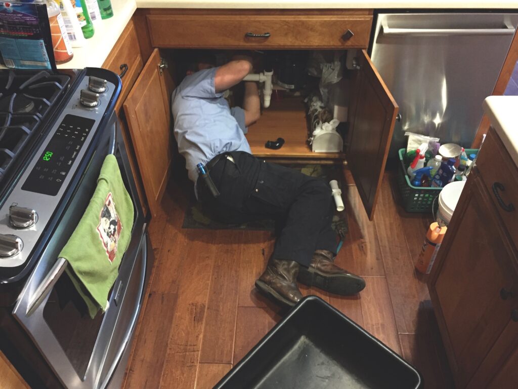 Man working under the kitchen sink fixing the plumbing.